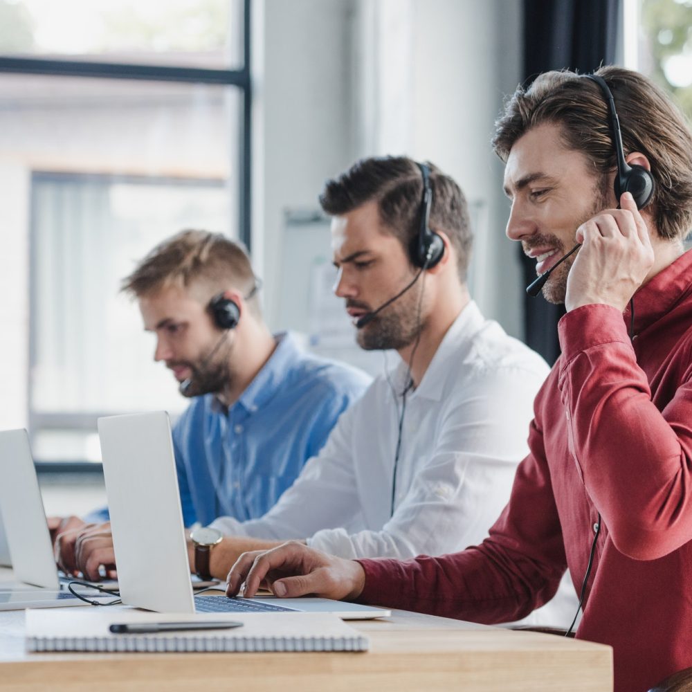 three-young-call-center-operators-in-headsets-using-laptops-in-office